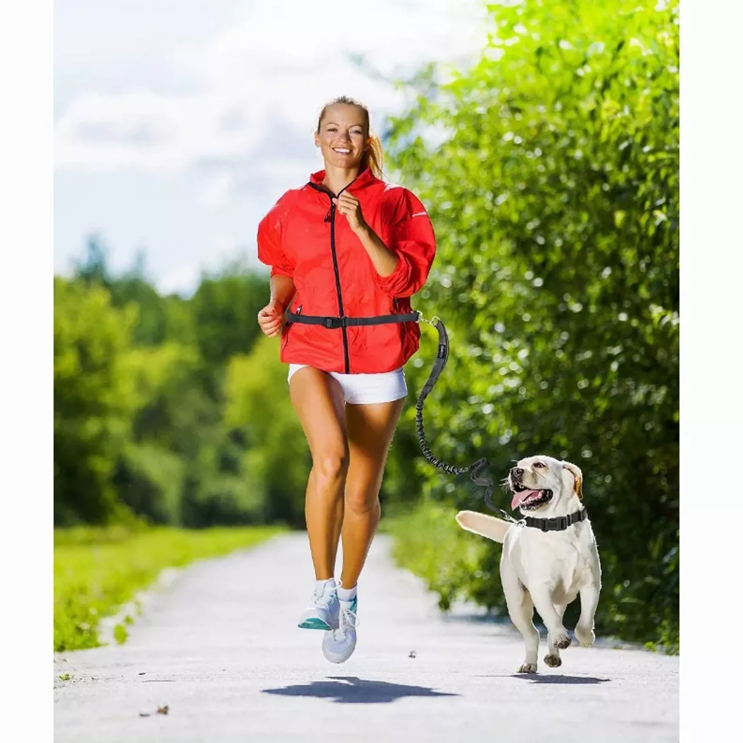 Woman in a red jacket running with a dog on a path surrounded by greenery