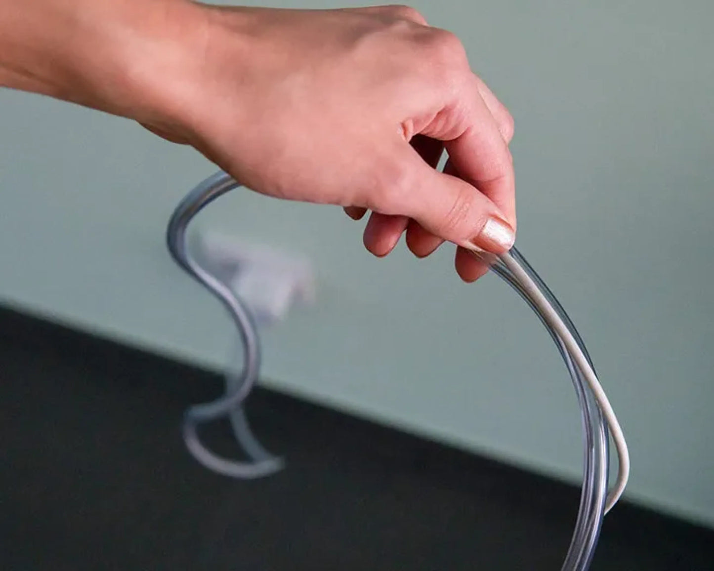 Hand holding a clear plastic hook against a neutral background