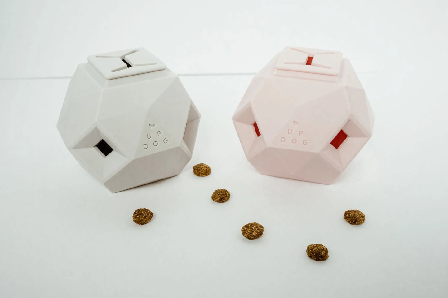 Two geometric pet toys on a white surface with scattered treats.