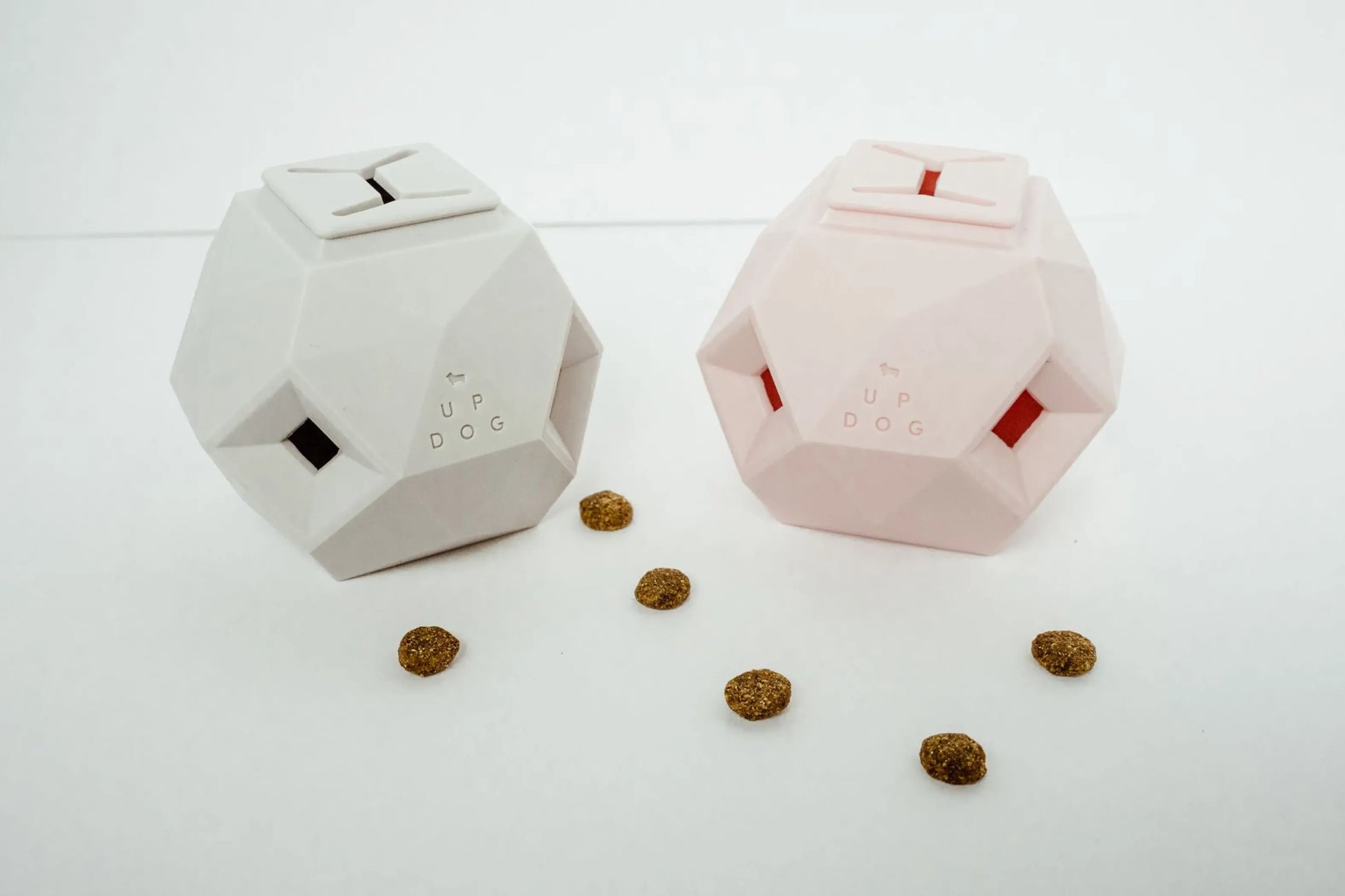 Two geometric pet toys on a white surface with scattered treats.