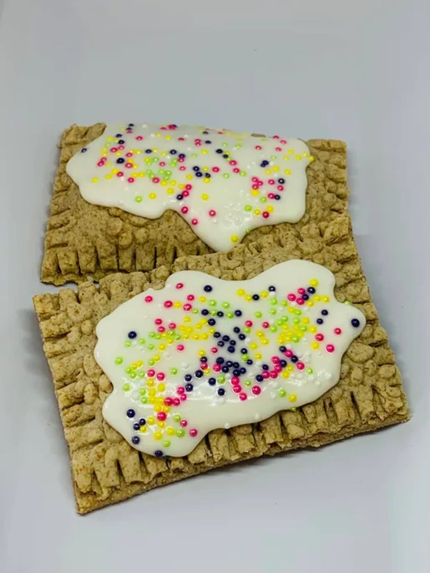 Two rectangular cookies with white icing and colorful sprinkles on a light gray background